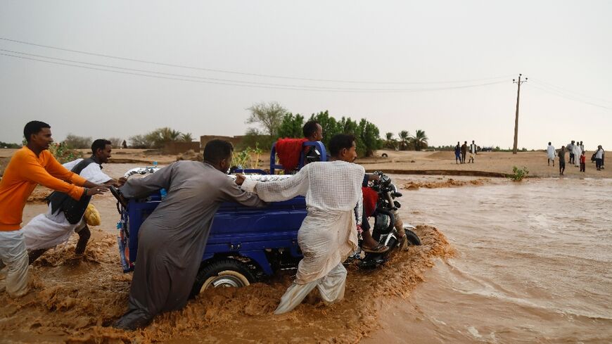 People push a vehicle through muddy flood water following torrential rains in Saqqai near Sudan's capital Khartoum