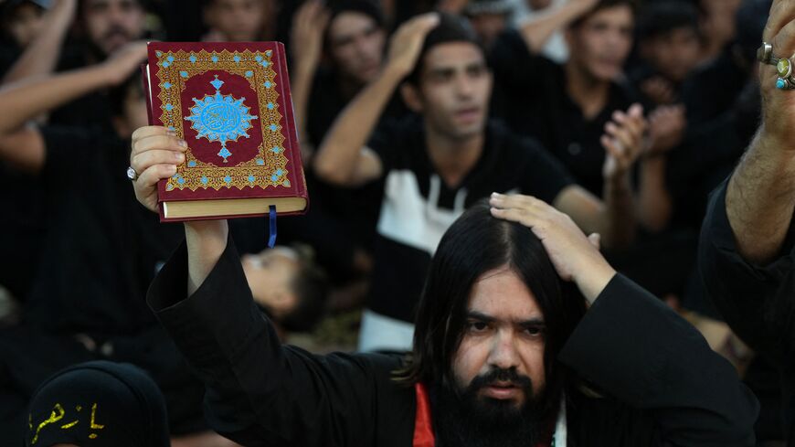 A Shiite Muslim man raises a Koran as he takes part in a mourning ritual in the city of Nasiriyah in Iraq's southern Dhi Qar province eraly on July 22, 2023, during the Muslim month of Muharram in the lead-up to Ashura. Ashura is a 10-day mourning period commemorating the seventh century killing of Prophet Mohammed's grandson Imam Hussein. (Photo by Asaad NIAZI / AFP) (Photo by ASAAD NIAZI/AFP via Getty Images)